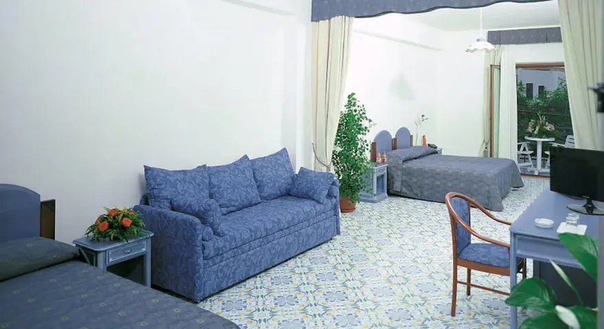 Camera spaziosa con divano blu, letti singoli e un letto matrimoniale. Pavimento decorato, tipico del **hotel club residence Martinica**.