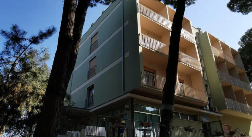 Edificio del pine beach hotel rosolina mare, con balconi e alberi di pino davanti.