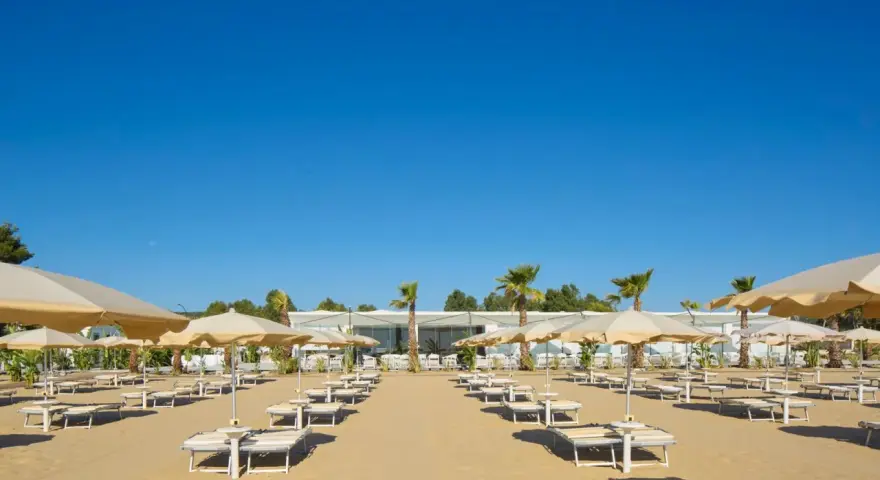 Filettate file di lettini e ombrelloni sulla sabbia dorata di Ripa Beach Vieste, sotto un cielo azzurro e limpido.