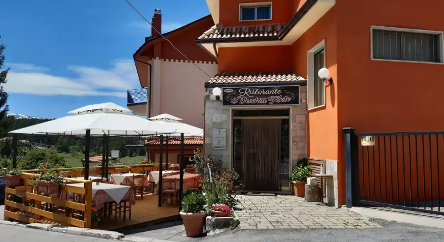 Ristorante La Vecchia Fonte, con tavoli all'aperto sotto ombrelloni bianchi, in una giornata di sole.