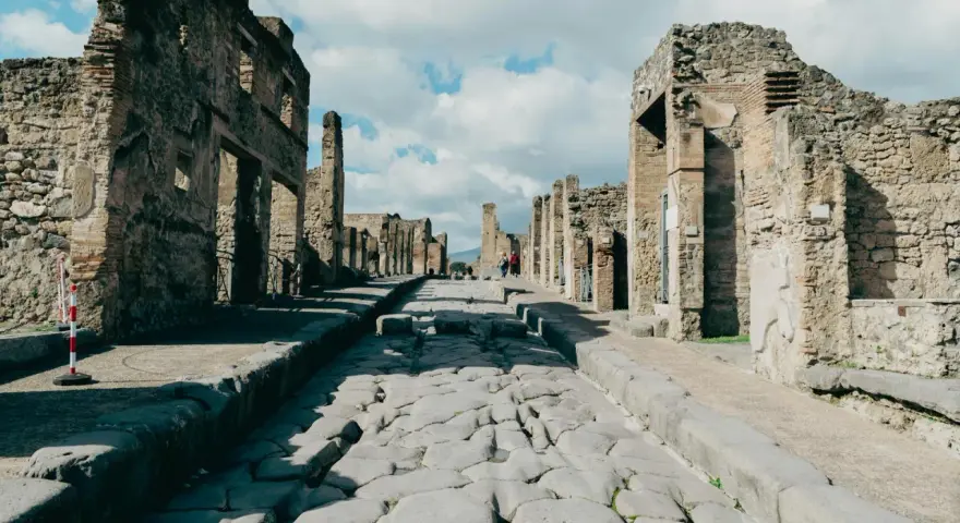 Antica strada romana a Pompei, con rovine di edifici e turisti che passeggiano. Un'ottima guida per come visitare Pompei.
