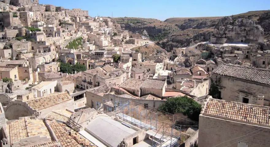 Panoramica dei Sassi di Matera, un **itinerario** suggestivo tra antiche case scavate nella roccia e tetti in cotto sotto un cielo azzurro.