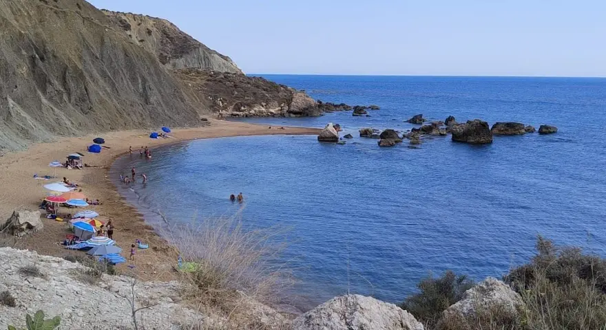 Spiaggia di Cala Vincenzina con scogliere, ombrelloni colorati e bagnanti che si godono il mare azzurro.
