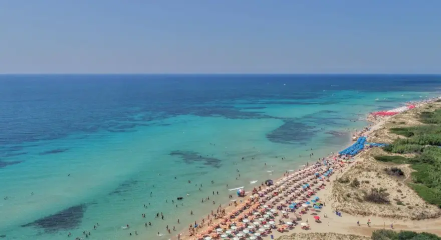Spiaggia affollata con ombrelloni colorati e gente che nuota nelle acque cristalline di Punta Prosciutto, le Maldive del Salento.