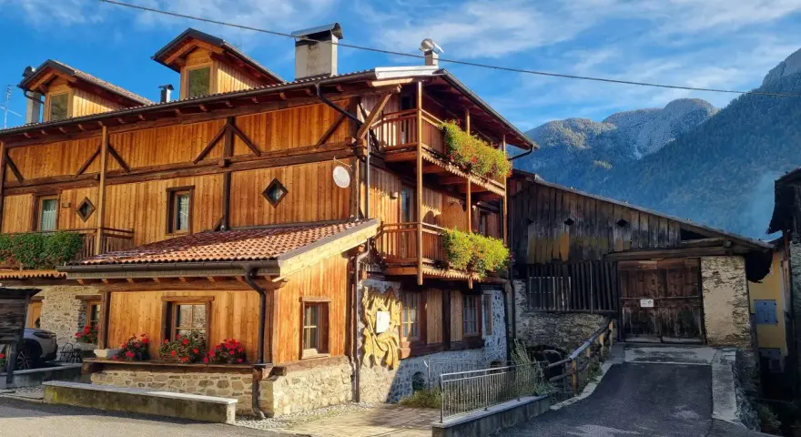 Casa in legno con balconi fioriti e montagne sullo sfondo. Un cartello "Alle Meridiane" indica un luogo incantevole a Lagopesole.