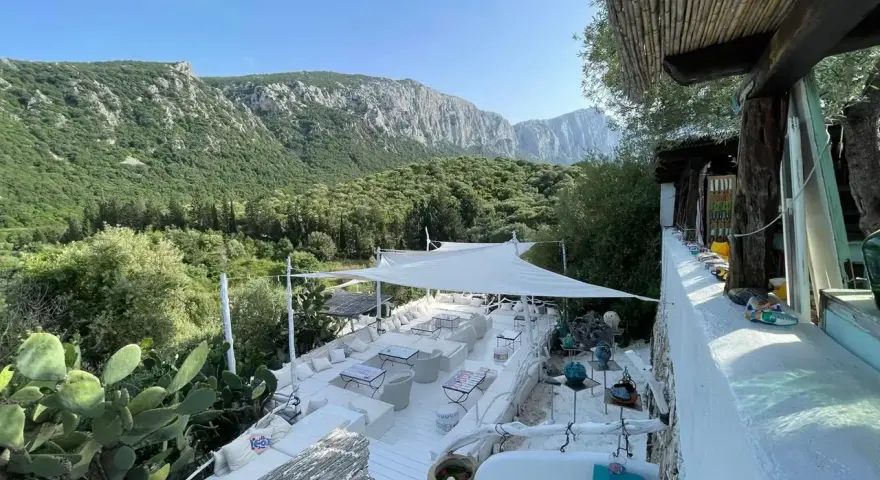 Terrazza panoramica con vista sui monti di Oliena, Sardegna. Arredamento bianco, cactus e vegetazione rigogliosa.