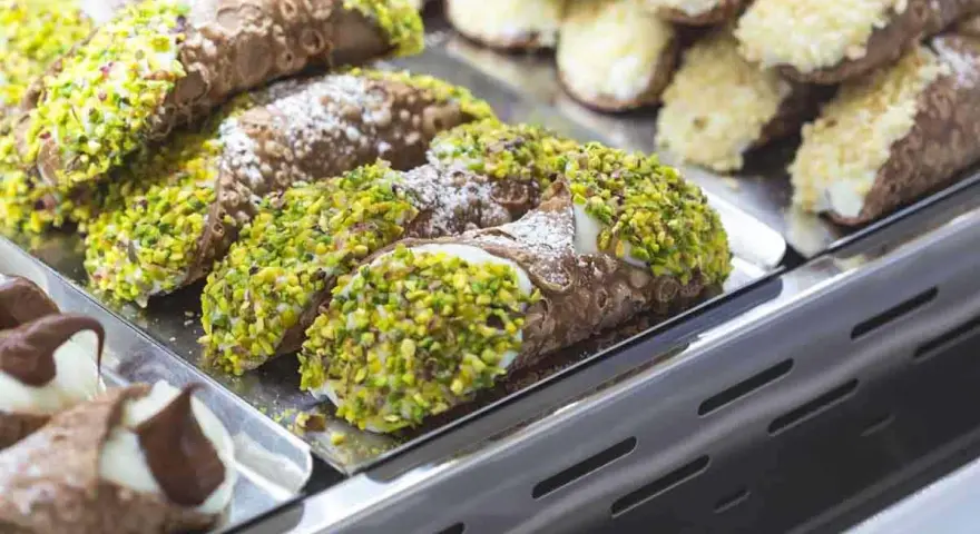 Cannoli siciliani, dolci tipici siciliani, ricoperti di pistacchi e zucchero a velo, in una vetrina.