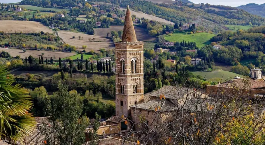 Campanile in borgo marchigiano, tra colline verdi e campi dorati, ideale per itinerari Marche autunnali.