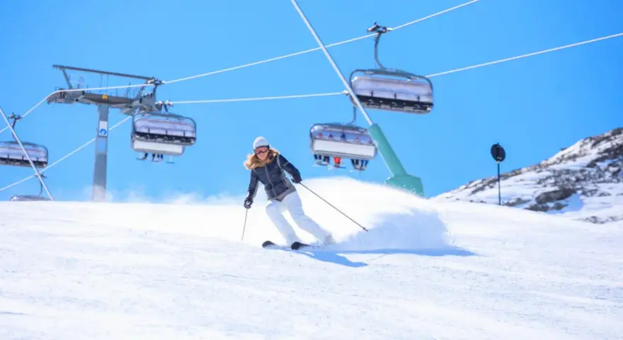 Donna scia su pendio innevato, con seggiovie sullo sfondo. Perfetta per la tua settimana bianca dove andare.