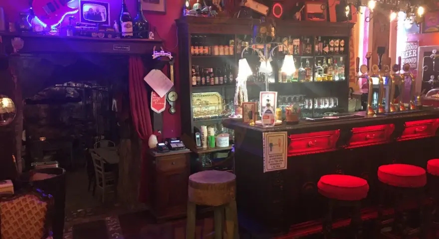 Interno della locanda del Principe a Artena, con chitarra elettrica luminosa, bancone bar e sgabelli rossi.