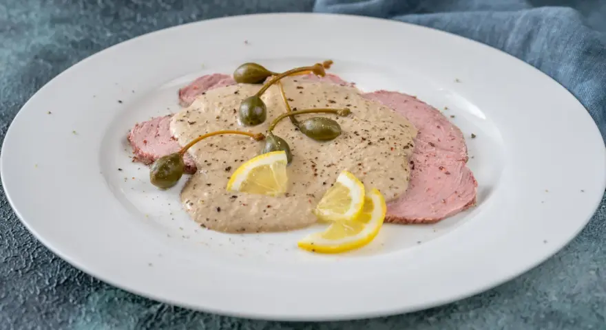 Vitello tonnato, uno dei piatti tipici di Torino, con fettine di carne rosa, salsa cremosa, capperi e limone.