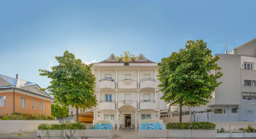 Hotel Marina Riccione: facciata bianca con insegna dorata, alberi verdi e fontane. Le recensioni lo descrivono come un'ottima scelta.