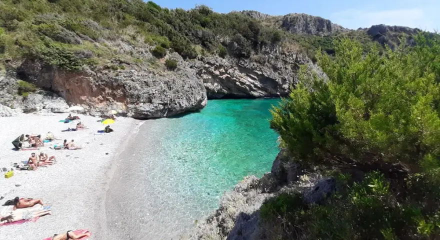 Spiaggia di ciottoli con gente che prende il sole e acque cristalline nel **Cilento mare**.