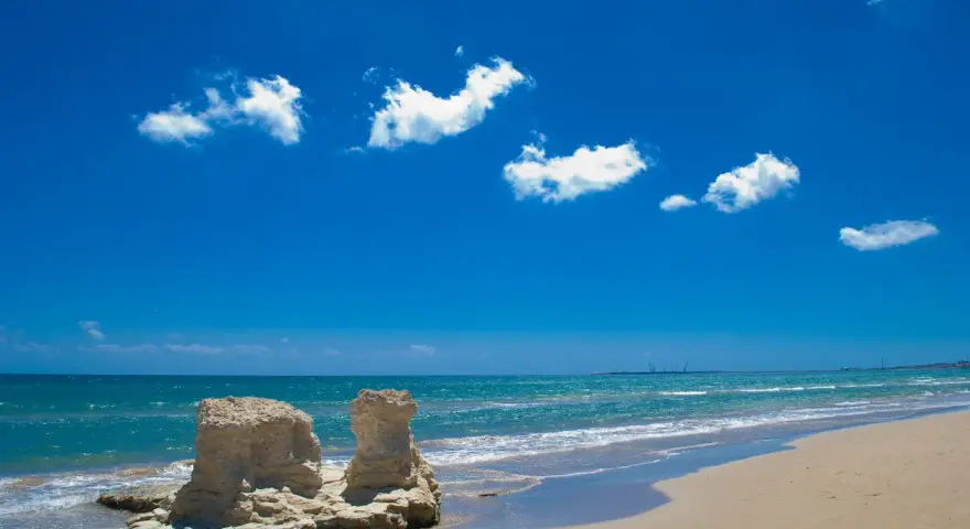 Spiagge bianche in Sicilia, con rocce scolpite dal mare e un cielo azzurro pieno di nuvole bianche.