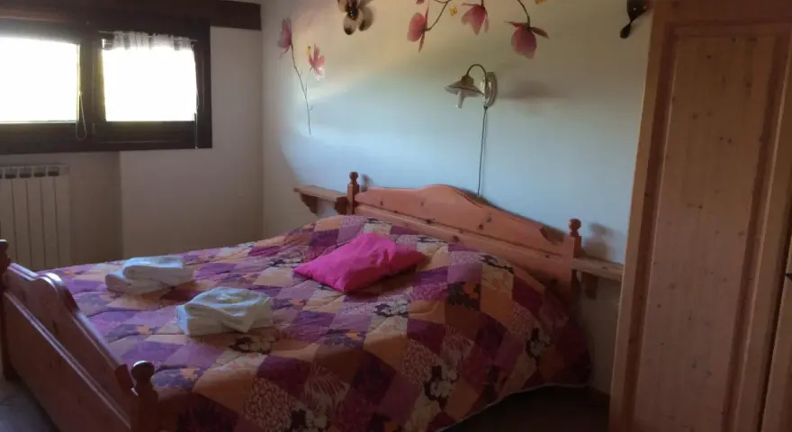 Camera accogliente in un agriturismo al Selvadigo, con letto, coperta colorata, cuscino rosa e decorazioni a farfalle e fiori sul muro.