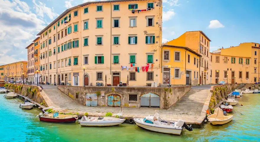 Canali di Livorno, cosa vedere in un giorno: case colorate affacciate sull'acqua, barche ormeggiate e panni stesi al sole.
