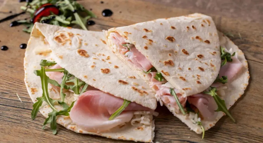 Piadina romagnola con prosciutto, rucola e formaggio. Un classico esempio di cosa si mangia in Emilia Romagna, semplice e gustosa.