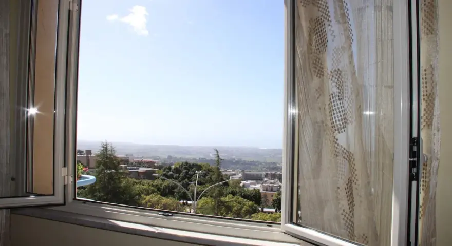 La terrazza sulla valle offre una vista panoramica su un paesaggio collinare con case e alberi verdi sotto un cielo azzurro.