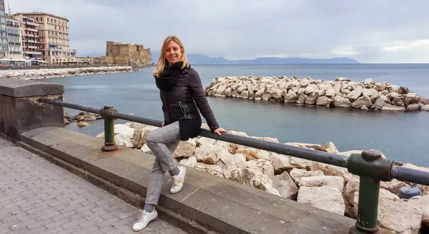 Donna sorridente sul lungomare di Napoli, con Castel dell'Ovo sullo sfondo. Perfetto per scoprire cosa vedere a Napoli in 3 giorni.
