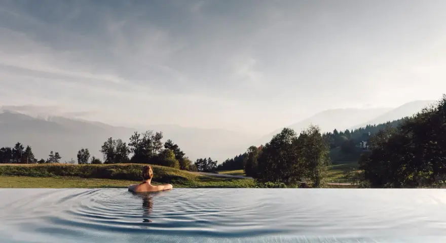 Donna rilassata in piscina a sfioro con vista sulle montagne, un'esperienza indimenticabile all'hotel Milla Montis.