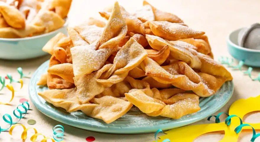 Dolci fritti a forma di fiocco, cosparsi di zucchero a velo, sono un classico di cosa si mangia a Carnevale in Italia.