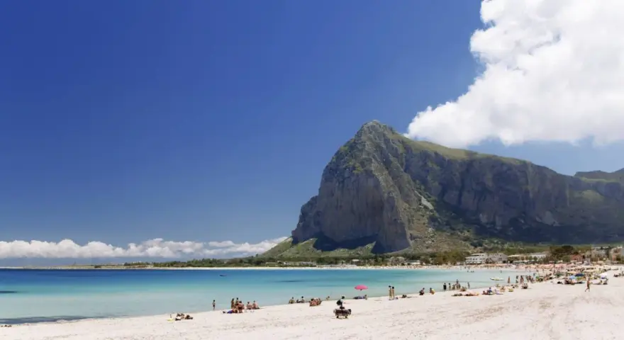 Spiaggia di San Vito Lo Capo, Sicilia, con il Monte Monaco imponente sullo sfondo e il mare cristallino che invita a un bagno.