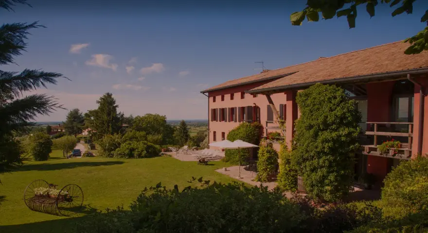 La casa rossa ai colli, immersa nel verde, offre un panorama incantevole. Un giardino curato con un antico attrezzo agricolo fiorito.