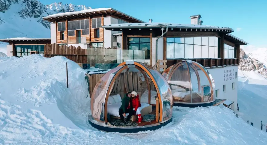 Coppia in una bolla trasparente innevata, perfetta idea su dove andare a gennaio in Italia per un soggiorno da sogno tra le montagne.