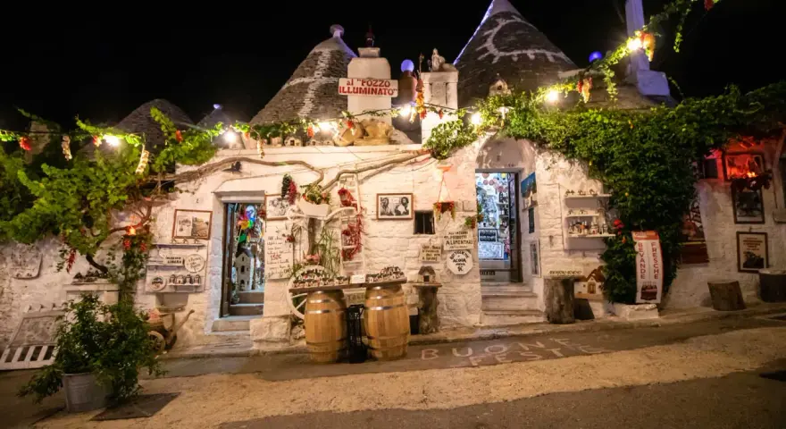 Trulli illuminati di notte ad Alberobello, con luci e decorazioni. Un invito a scoprire le cose da fare a Alberobello, tra negozi e prodotti tipici.