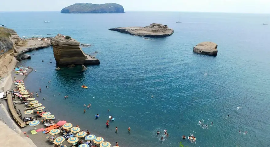 Le **spiagge** di Ventotene, con ombrelloni colorati e bagnanti in un mare azzurro, fanno da cornice a scogli suggestivi e all'isola di Santo Stefano in lontananza.