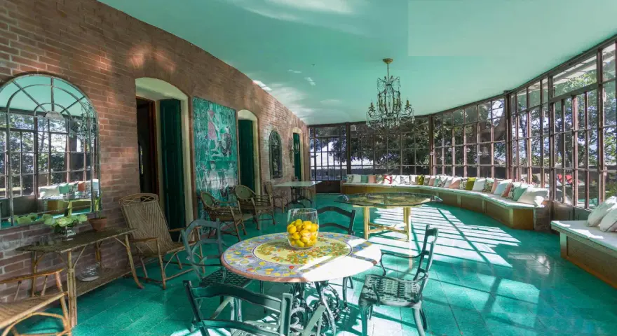 Veranda luminosa della villa dei cipressi a Sona, con pavimenti verdi, mobili in vimini e un grande divano curvo con cuscini colorati.