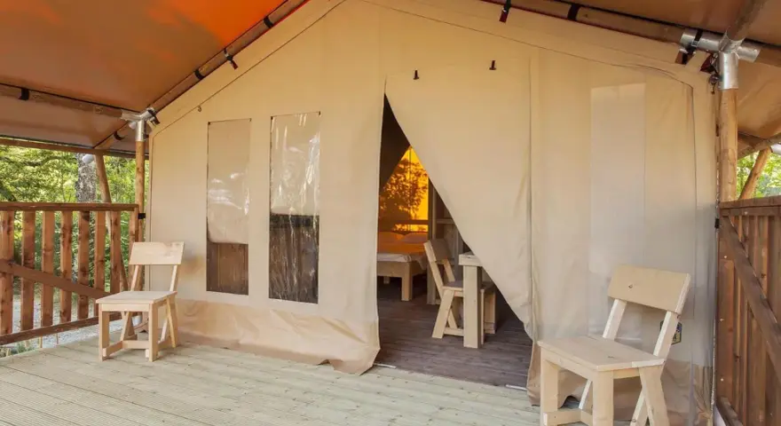 Tenda accogliente nel Luxor Chianti Glamping Village, con sedie in legno sulla veranda e vista sull'interno arredato.