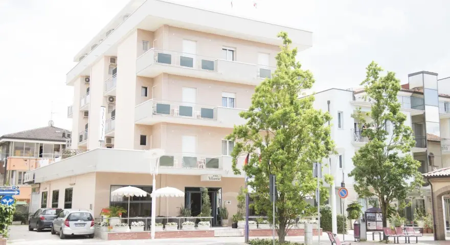 Hotel Atlantic Igea Marina: scopri i prezzi per la tua vacanza al mare. Edificio moderno con alberi verdi davanti.