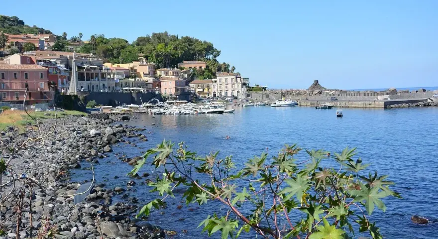 Il lungomare di Acireale, con case colorate, barche ormeggiate e il mare azzurro.