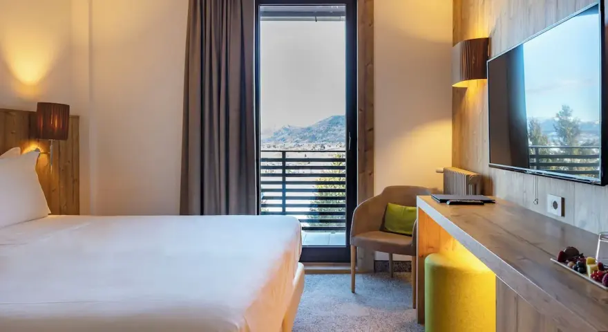 Camera accogliente con vista panoramica, tipica del Linta Hotel Asiago. Letto comodo, poltrona e balcone con paesaggio montano.