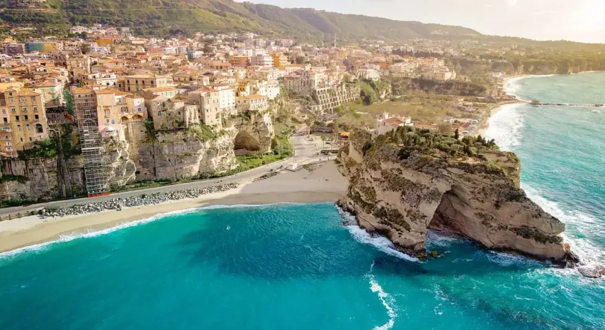 Panoramica mozzafiato delle **calabrie spiagge** con case colorate aggrappate alle scogliere e un mare turchese.