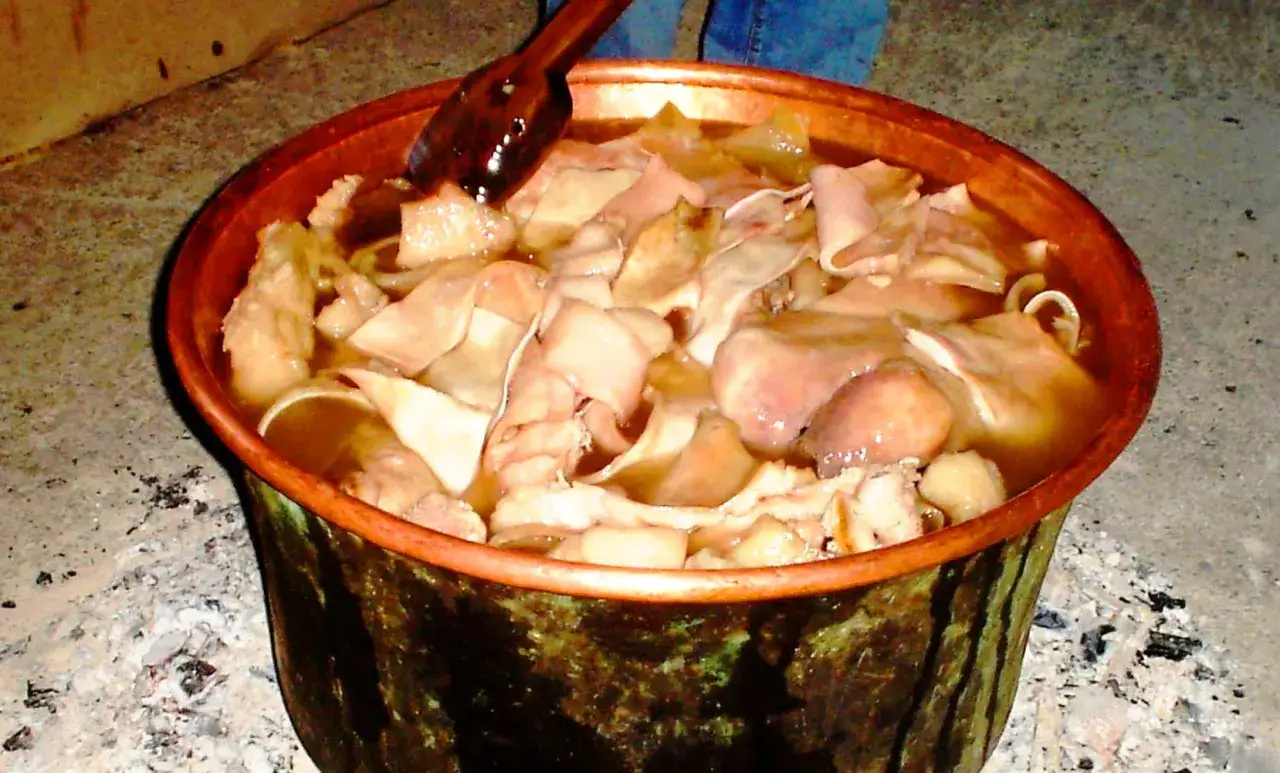 Un pentolone di rame pieno di cibo calabrese, con pezzi di carne e brodo fumante.
