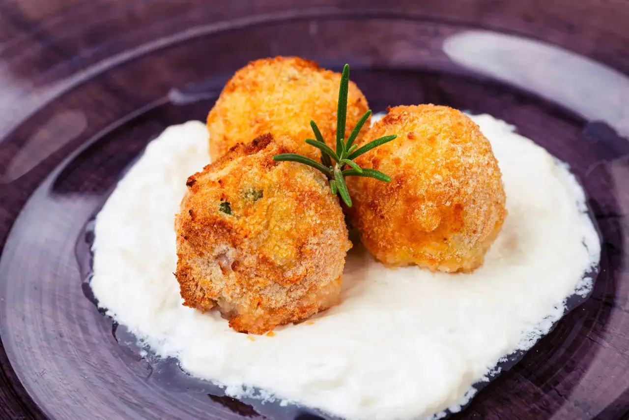 Arancini dorati su crema bianca, un'idea sfiziosa su cosa mangiare a Catania.