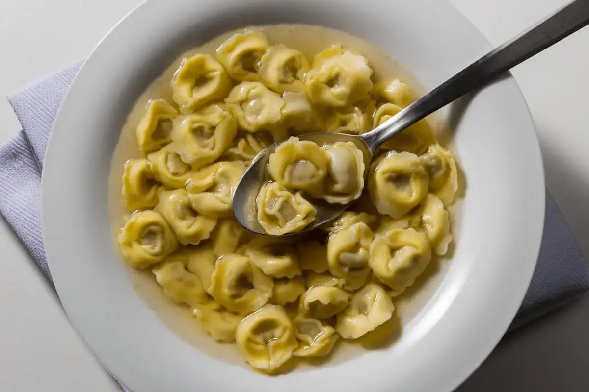 Tortellini in brodo, uno dei piatti tipici di Ravenna, serviti in una ciotola bianca con un cucchiaio.