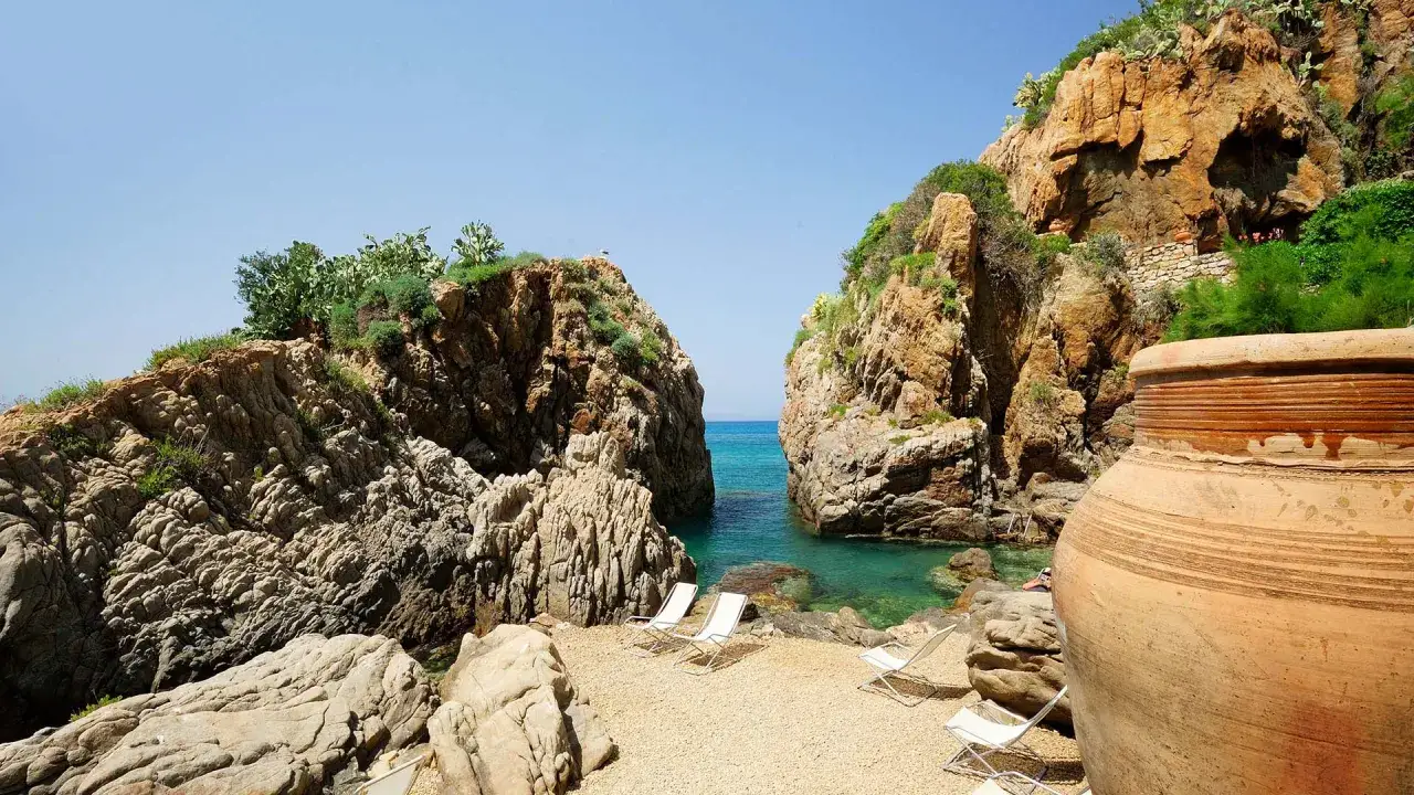 Spiaggia di Cala Vincenzina con rocce imponenti, mare cristallino e lettini pronti per il relax.