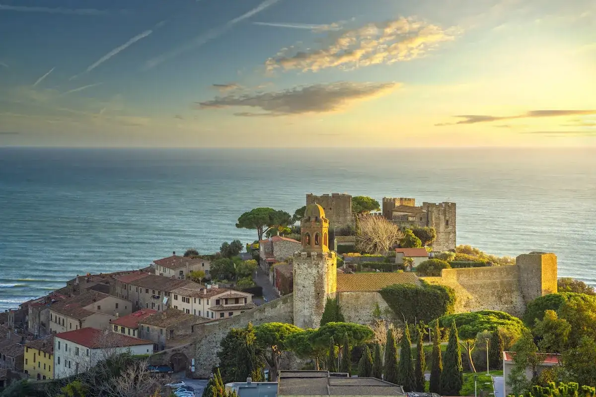 Castiglione della Pescaia: cosa vedere? Un borgo medievale con castello e torre campanaria affacciato sul mare, incantevole al tramonto.