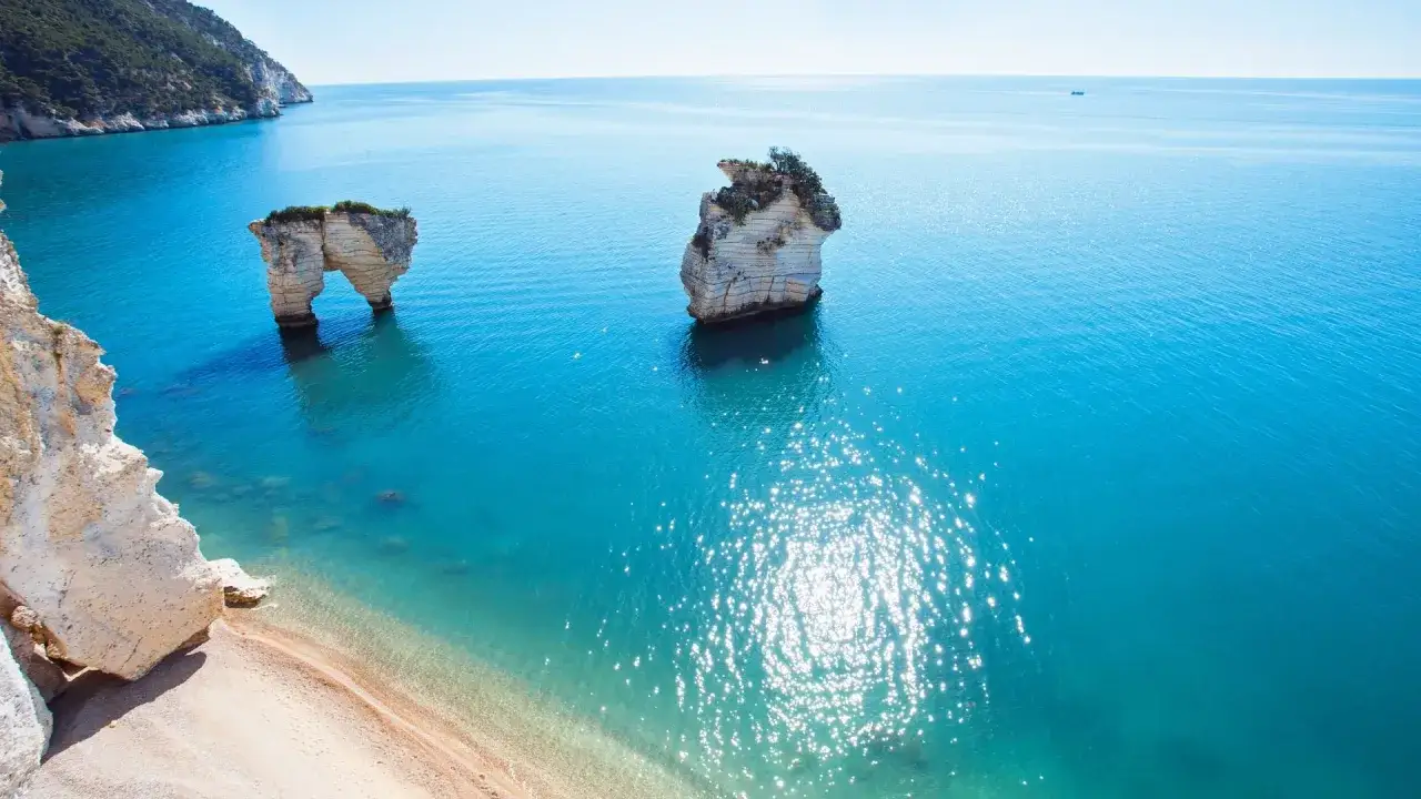 Scogliere bianche e mare cristallino a Peschici, con faraglioni che emergono dall'acqua turchese.