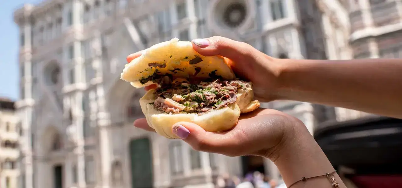 Un panino con lampredotto, un classico su cosa mangiare a Firenze, tenuto in mano con il Duomo sullo sfondo.