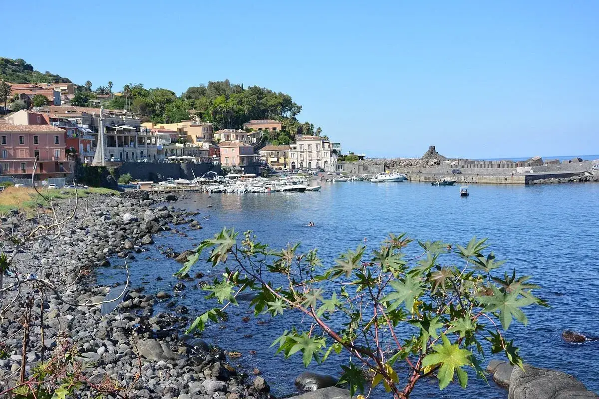 Il lungomare di Acireale con case colorate, barche ormeggiate e il mare blu.
