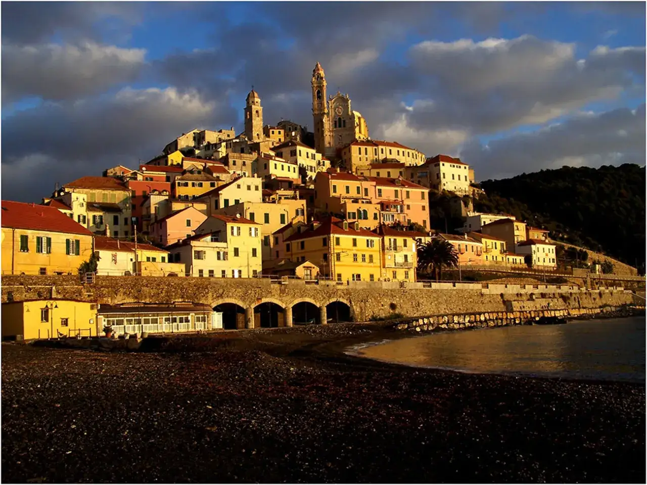 Borgo colorato arroccato sulla collina, con campanile imponente, affacciato sul mare delle coste liguri.