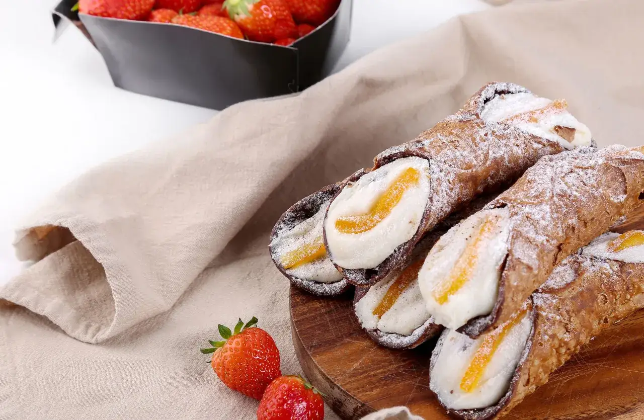 Cannoli ripieni di crema e canditi, dolci tipici siciliani, su tagliere di legno con fragole fresche e tovagliolo di lino.