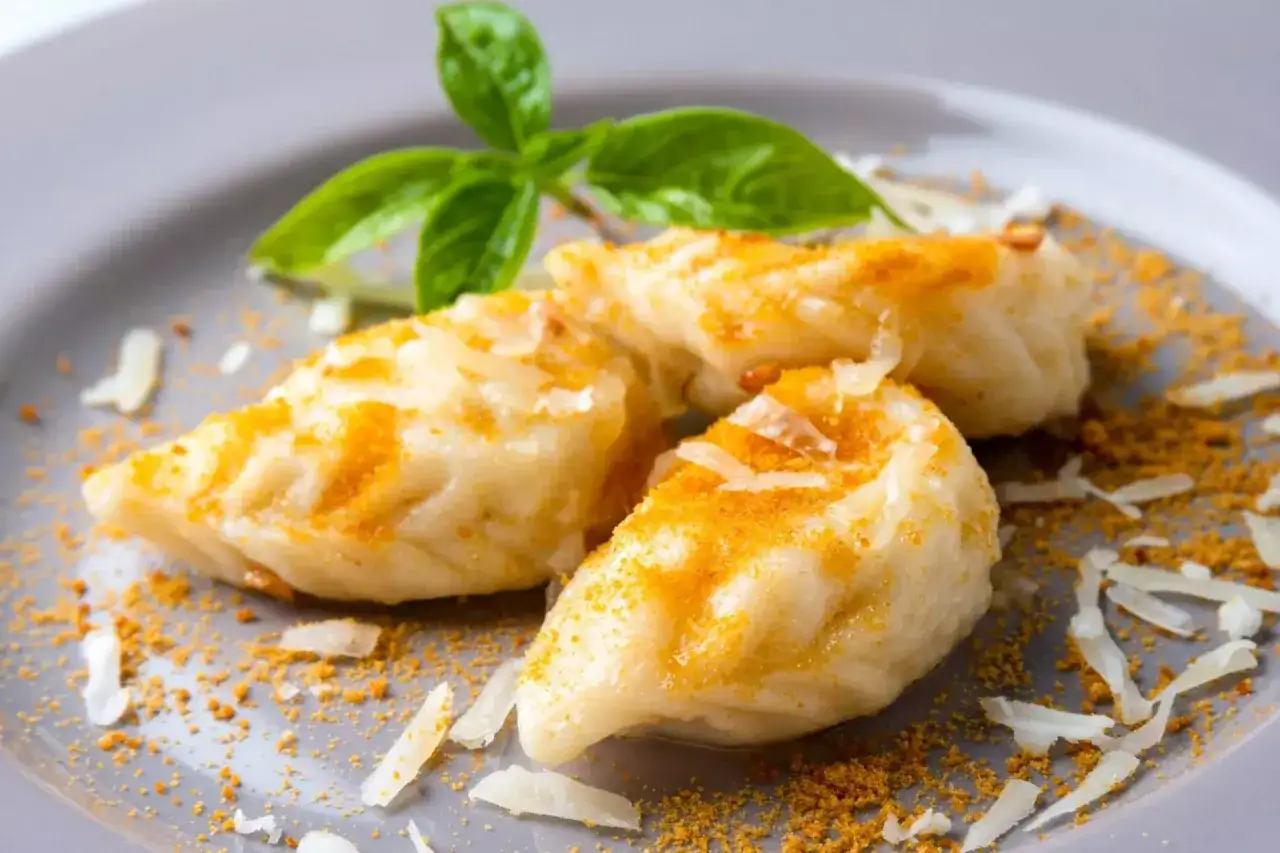 Tre culurgiones, un delizioso cibo tipico sardo, conditi con formaggio grattugiato e una spolverata di spezie, guarniti con basilico fresco.