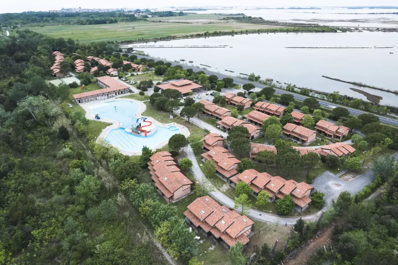 Villaggio Ca' Laguna: complesso residenziale con piscina e scivoli, circondato da verde e affacciato su una laguna.