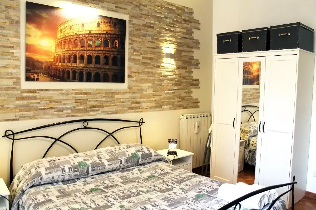 Camera da letto con quadro del Colosseo, che ricorda il Boscolo Circo Massimo. Parete in pietra, letto matrimoniale e armadio bianco.