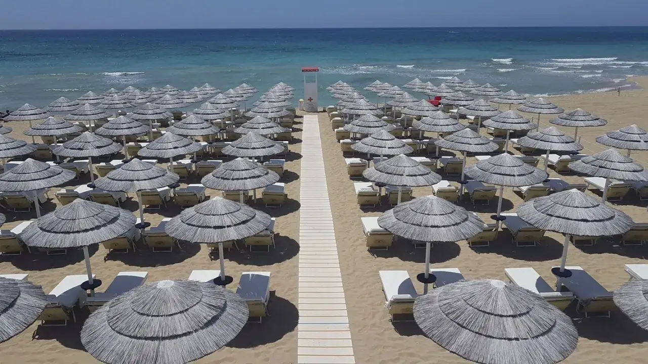 Filettato di ombrelloni e lettini sulla sabbia dorata, con il mare azzurro sullo sfondo. Un'oasi di relax al mamire lido marini.